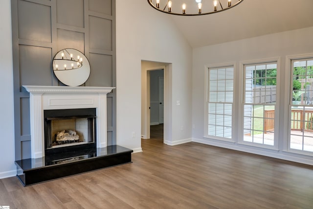 unfurnished living room with high vaulted ceiling, a notable chandelier, and wood finished floors