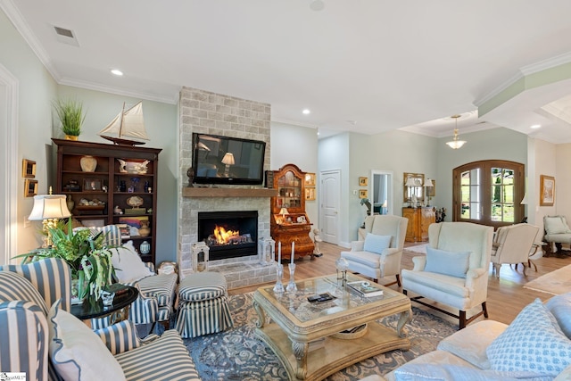 living area with a fireplace, wood finished floors, visible vents, and ornamental molding