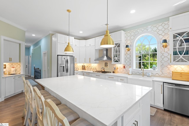 kitchen featuring a sink, tasteful backsplash, wall chimney range hood, crown molding, and appliances with stainless steel finishes