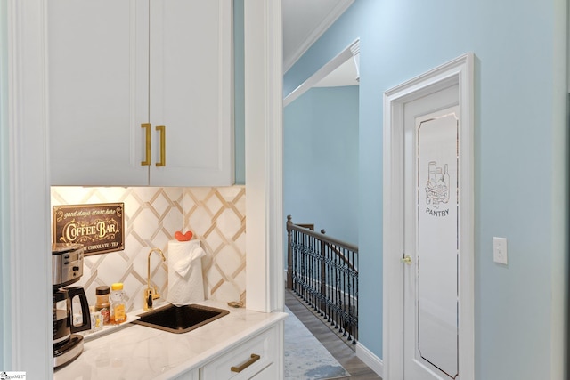 bar with backsplash, wood finished floors, a sink, crown molding, and indoor wet bar