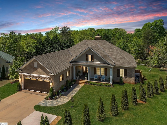 view of front facade with an attached garage, a lawn, covered porch, and driveway