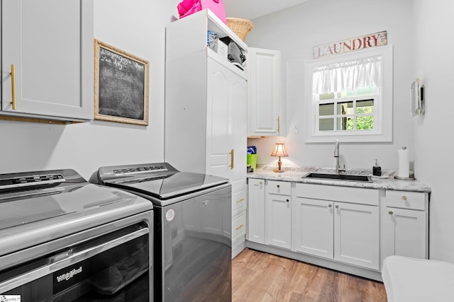 laundry area featuring cabinet space, washer and clothes dryer, light wood finished floors, and a sink