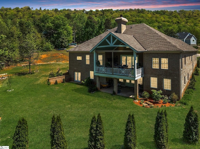 rear view of property featuring a patio area, a lawn, and a chimney