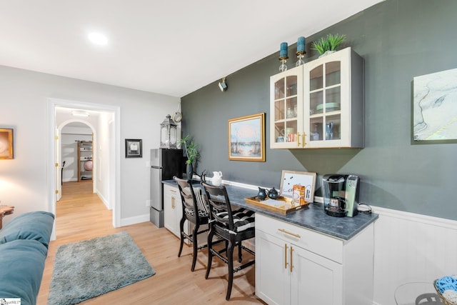 home office featuring arched walkways, light wood-style floors, built in study area, and wainscoting