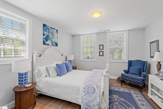 bedroom featuring visible vents, baseboards, wood finished floors, and multiple windows