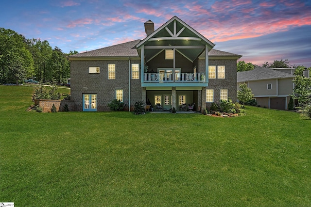 back of property at dusk with brick siding, a yard, french doors, and a chimney