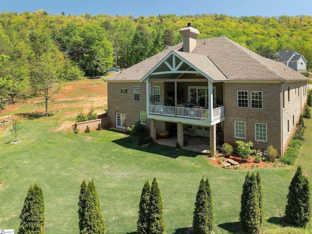 back of house with a lawn, a chimney, and a wooded view