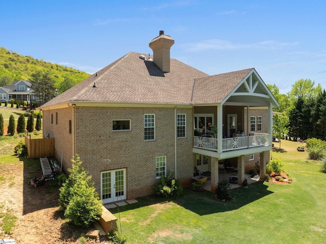 rear view of house with a lawn, brick siding, a chimney, and french doors