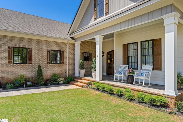 doorway to property with brick siding, a yard, a shingled roof, and covered porch