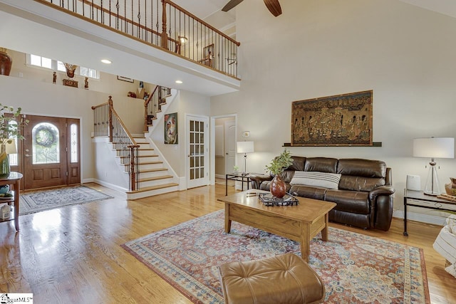 living area featuring baseboards, a ceiling fan, wood finished floors, a high ceiling, and stairway