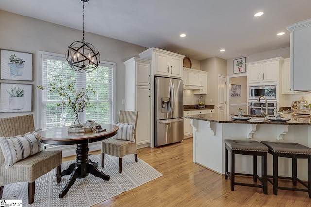 kitchen with dark stone counters, light wood-type flooring, recessed lighting, a notable chandelier, and appliances with stainless steel finishes
