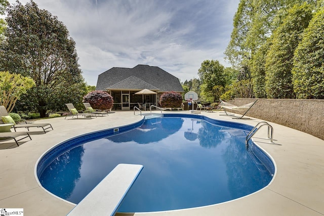 outdoor pool with a diving board and a patio