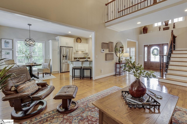 living room with light wood-style floors, stairway, a high ceiling, and a healthy amount of sunlight