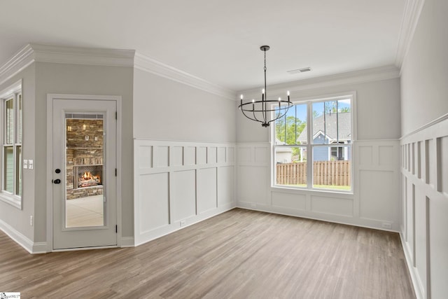 unfurnished dining area with crown molding, wood finished floors, a chandelier, and a decorative wall