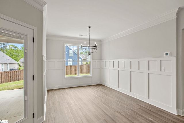 unfurnished dining area with a decorative wall, crown molding, a chandelier, and light wood-style floors