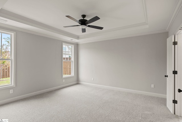carpeted spare room with a raised ceiling, crown molding, baseboards, and a ceiling fan