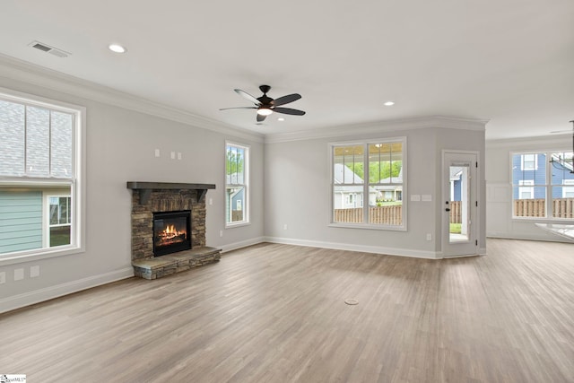 unfurnished living room with a stone fireplace, visible vents, light wood-style floors, crown molding, and ceiling fan with notable chandelier