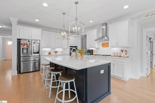 309 Nebbiolo Ln, Simpsonville, SC 29681 - kitchen with appliances with stainless steel finishes, wall chimney range hood, light wood-type flooring, a center island with sink, and white cabinetry
