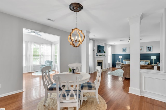 dining room with ceiling fan with notable chandelier, visible vents, a fireplace, and wood-type flooring