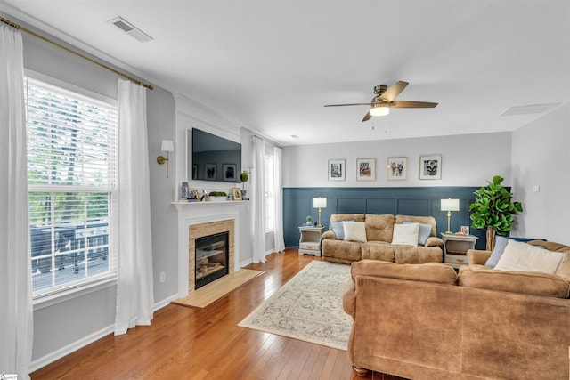 living room with hardwood / wood-style floors, a glass covered fireplace, visible vents, and ceiling fan