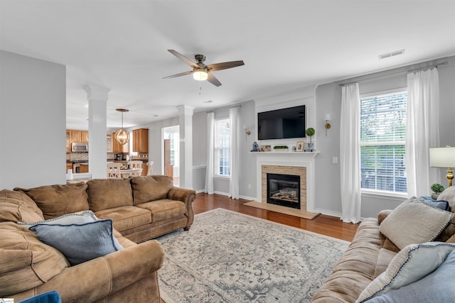 living area with decorative columns, baseboards, visible vents, wood finished floors, and ceiling fan
