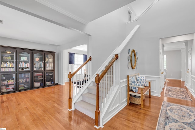 stairs with a wainscoted wall, wood finished floors, and crown molding