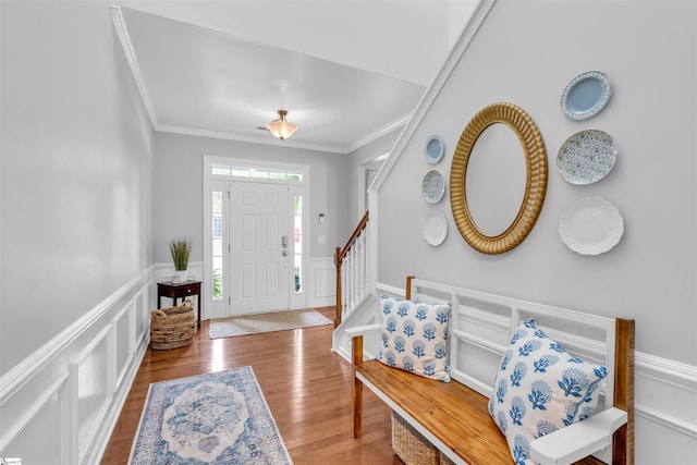 foyer entrance with stairway, a decorative wall, crown molding, wood finished floors, and wainscoting