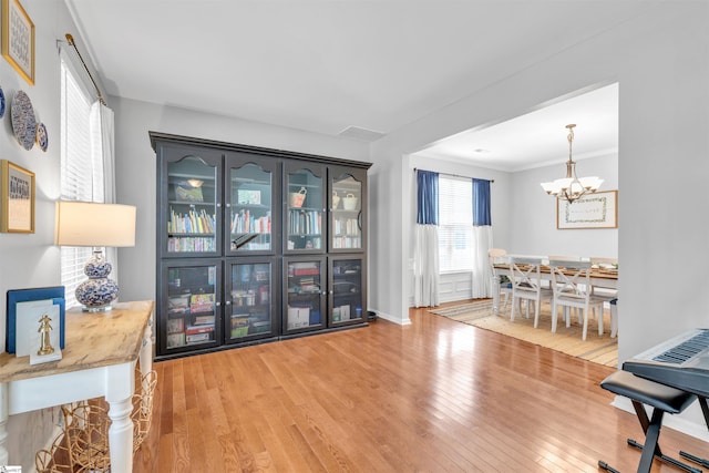 interior space featuring light wood-type flooring, baseboards, a notable chandelier, and ornamental molding