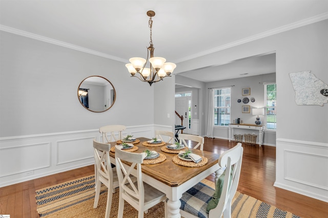 dining space featuring stairway, a wainscoted wall, wood finished floors, crown molding, and a notable chandelier