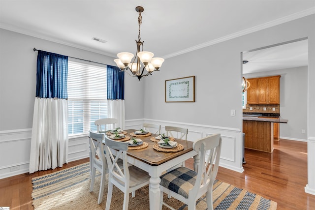 dining room with wainscoting, light wood-style flooring, a chandelier, and ornamental molding
