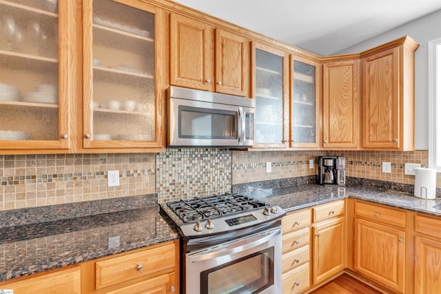 kitchen with tasteful backsplash, dark stone countertops, stainless steel appliances, and glass insert cabinets