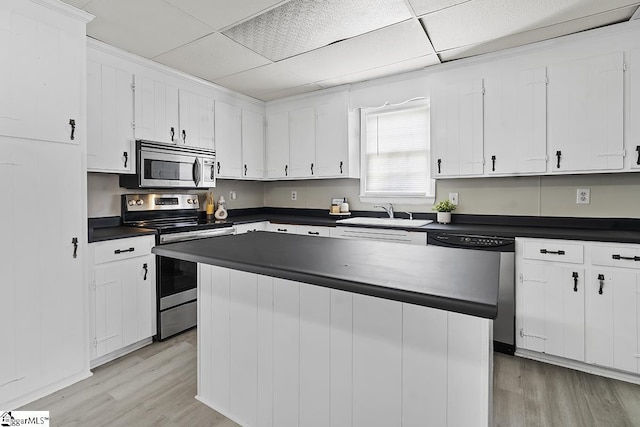 kitchen featuring light wood finished floors, stainless steel appliances, dark countertops, a sink, and white cabinetry