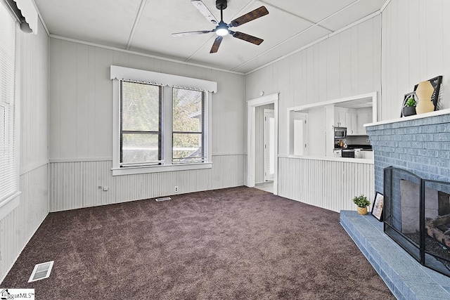 living area with wooden walls, visible vents, a brick fireplace, carpet flooring, and ceiling fan