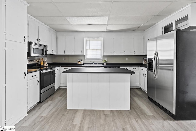 kitchen featuring light wood finished floors, stainless steel appliances, a paneled ceiling, and dark countertops