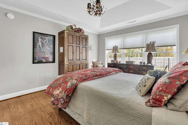 bedroom with an inviting chandelier, a tray ceiling, wood finished floors, visible vents, and baseboards