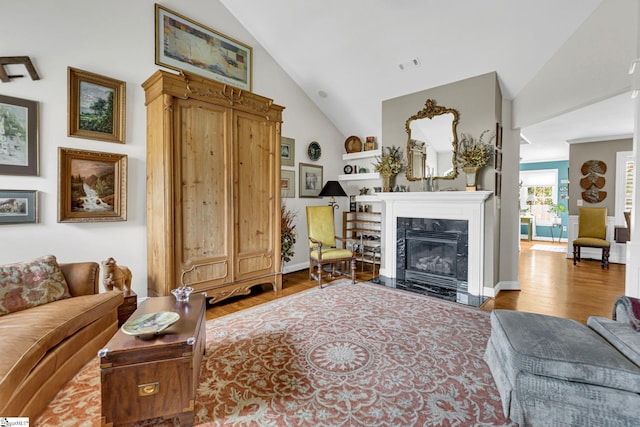 living room featuring a high end fireplace, lofted ceiling, wood finished floors, and visible vents