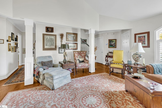 living area featuring lofted ceiling, stairway, wood finished floors, crown molding, and decorative columns