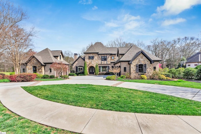 french country style house with a front lawn, stone siding, and curved driveway