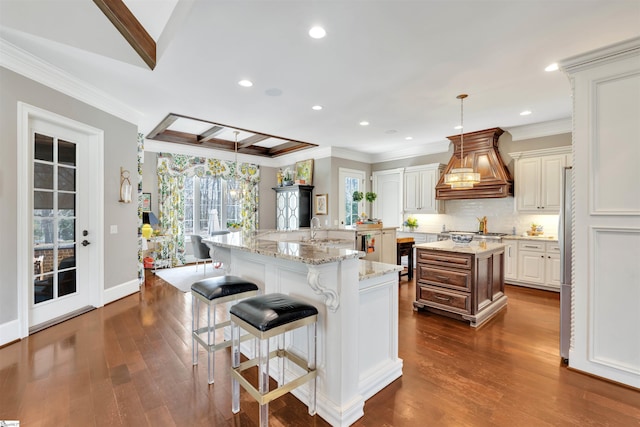 kitchen with a spacious island, custom exhaust hood, decorative light fixtures, dark wood-type flooring, and ornamental molding