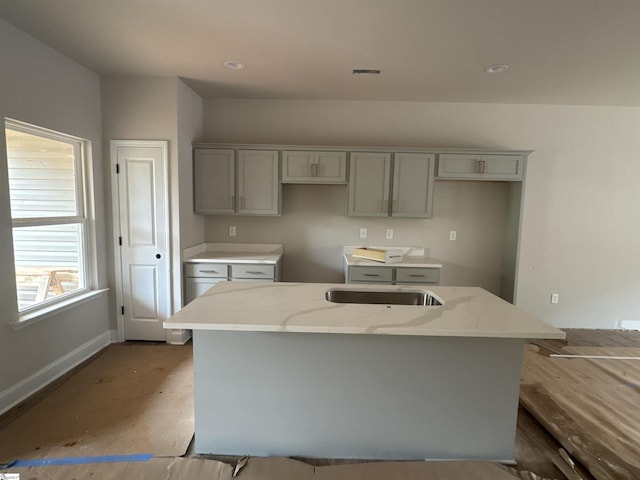 kitchen featuring light stone counters, baseboards, gray cabinetry, visible vents, and a kitchen island