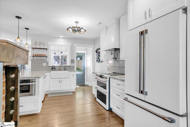 kitchen with a sink, tasteful backsplash, white cabinetry, white appliances, and premium range hood