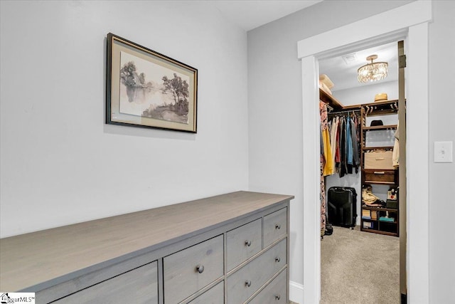 spacious closet with carpet floors and an inviting chandelier