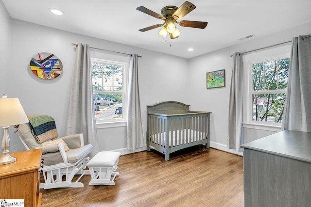 bedroom featuring light wood-style flooring, baseboards, a nursery area, and multiple windows