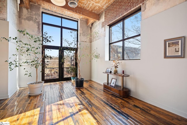 entrance foyer with a high ceiling, visible vents, wood-type flooring, beam ceiling, and baseboards