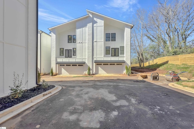 rear view of house featuring fence, an attached garage, aphalt driveway, and stucco siding