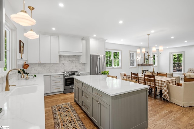 kitchen featuring light wood finished floors, a sink, backsplash, gray cabinets, and appliances with stainless steel finishes