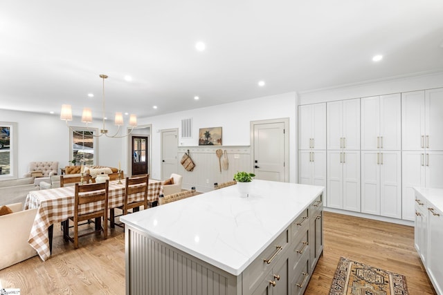 kitchen with light wood finished floors, a center island, open floor plan, gray cabinetry, and light stone counters