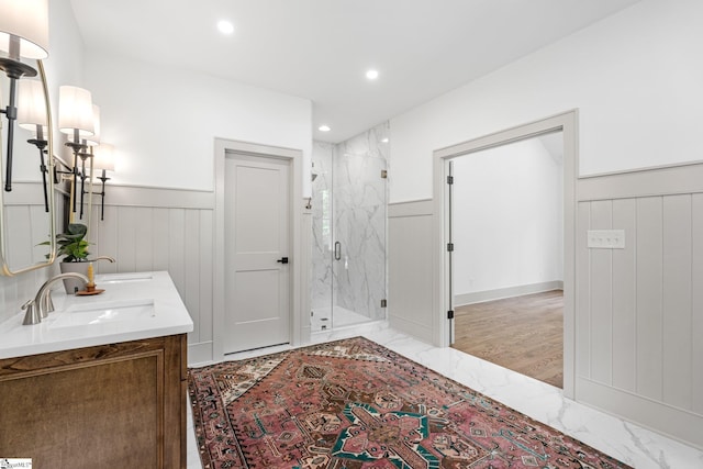 bathroom with marble finish floor, a marble finish shower, a sink, a decorative wall, and wainscoting