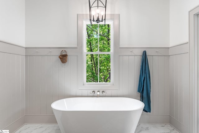 bathroom with marble finish floor, a freestanding bath, and a wainscoted wall