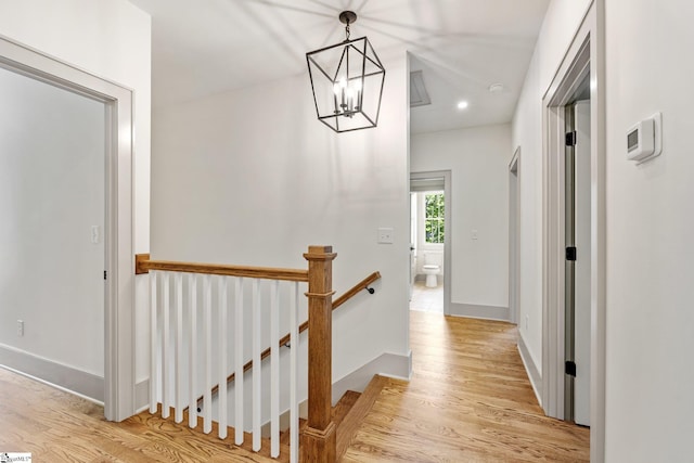 hallway with light wood finished floors, baseboards, an inviting chandelier, and an upstairs landing